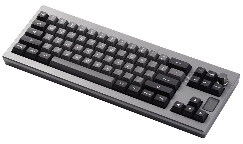 Na obrazie widoczna jest klawiatura mechaniczna w kolorze czarno-srebrnym z klawiszami oznaczonymi literami i symbolami. Klawiatura posiada pokrętło w prawym górnym rogu oraz dodatkowe klawisze funkcyjne.