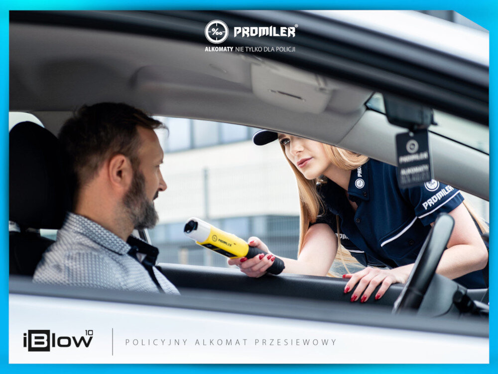 Kobieta w mundurze trzyma alkomat iBlow, podając go mężczyźnie siedzącemu w samochodzie. Widoczne logo \'PROMILER\' oraz tekst \'ALKOMATY. NIE TYLKO DLA POLICJI\' i \'POLICYJNY ALKOMAT PRZESIEWOWY\'.