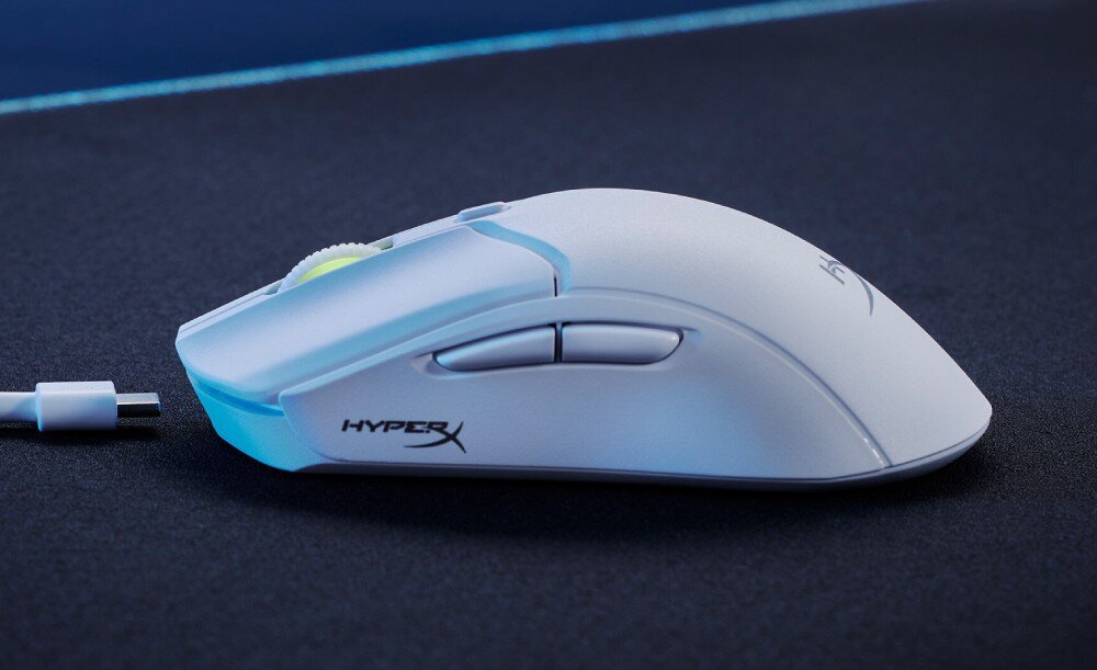 Biała mysz komputerowa z logo \'HYPERX\' na boku, umieszczona na ciemnej powierzchni. Obok myszy widoczny jest biały kabel USB.