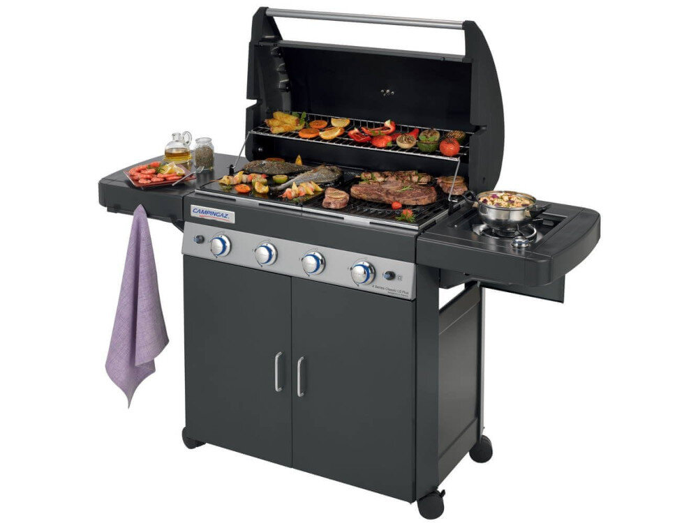 Grill ogrodowy gazowy z otwartą pokrywą, na ruszcie znajdują się różnorodne potrawy. Na panelu przednim widoczne są pokrętła oraz logo \'CAMPINGAZ\'.