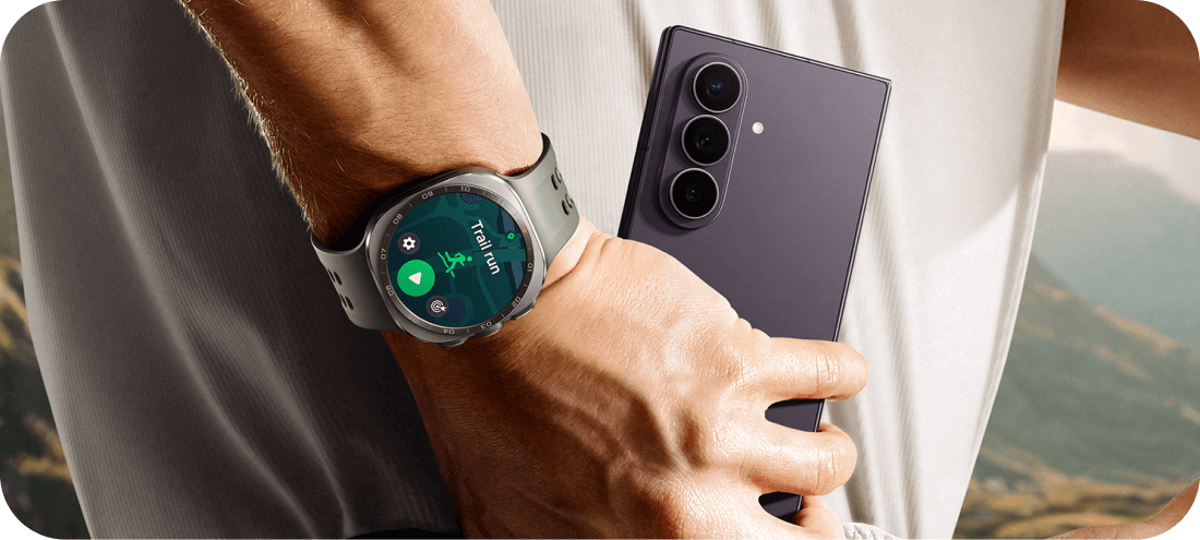 Galaxy Watch Ultra2 na nadgarstku i Galaxy Z Fold8 Ultra trzymany w dłoni. Osoba trzyma smartfon z trzema aparatami z tyłu, a na nadgarstku ma zegarek z wyświetlaczem pokazującym ikonę biegania i napis \'10:08\'.