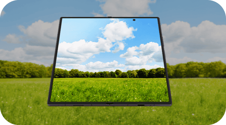 Rozłożony Galaxy Z Fold8 Ultra z jasnym ekranem na tle zielonej łąki. Obraz przedstawia ekran urządzenia wyświetlający krajobraz z zieloną łąką i niebieskim niebem z białymi chmurami. W tle widoczne są drzewa.