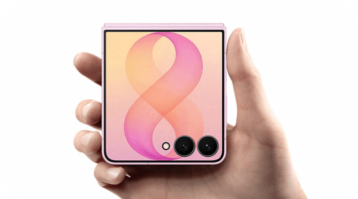 Różowy Galaxy Z Flip8 trzymany w dłoni, z ekranem zewnętrznym i dwoma aparatami. Osoba trzyma złożony różowy smartfon z widocznym ekranem, na którym jest gradientowy symbol przypominający cyfrę 8. W dolnym rogu znajdują się dwa obiektywy aparatu i mały czujnik.