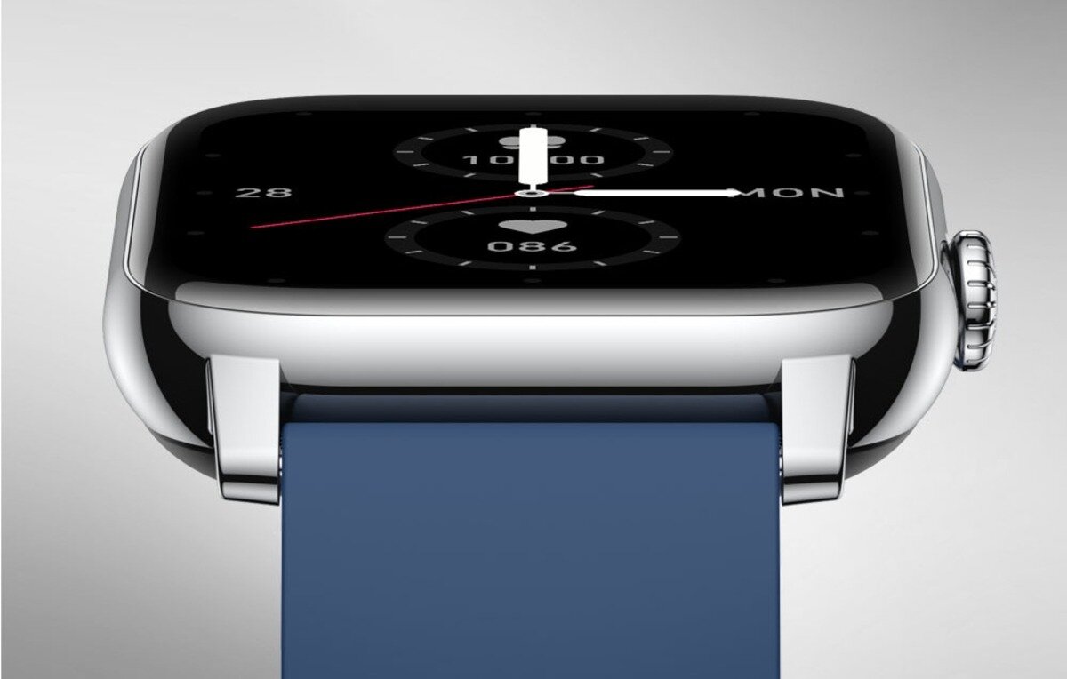 Srebrny smartwatch z niebieskim paskiem, wyświetlający tarczę z białymi wskazówkami i cyframi. Na ekranie widoczne są liczby 28, 10000, 086 oraz napis MON.