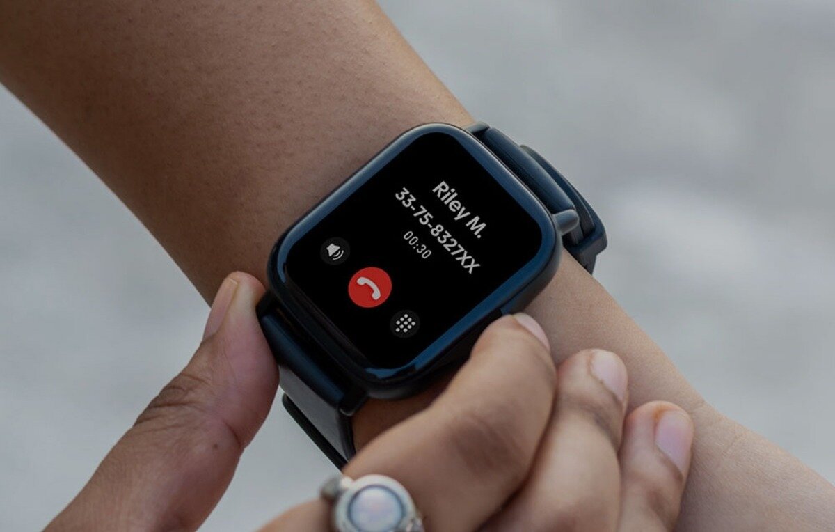 Osoba nosi smartwatch z wyświetlaczem pokazującym ekran połączenia z tekstem: \'Riley M. 33-75-832XX 00:30\'.