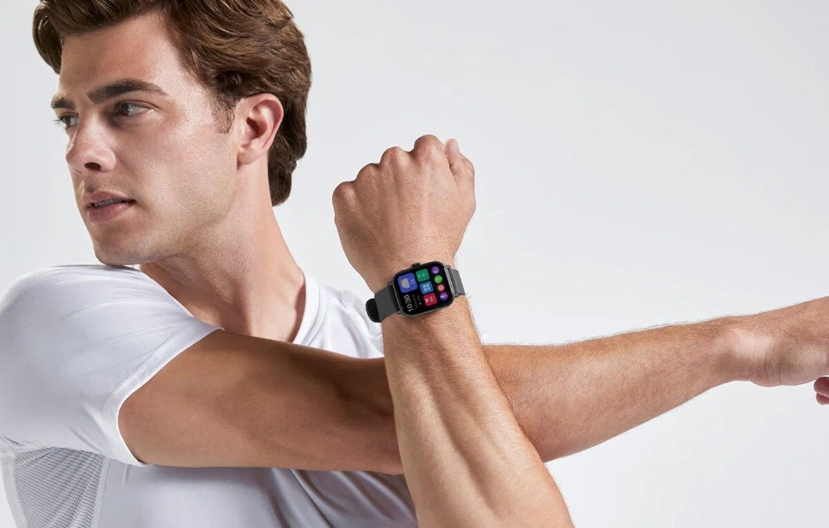 Osoba w białej koszulce prezentuje smartwatch na nadgarstku, z kolorowym wyświetlaczem pokazującym różne ikony aplikacji.