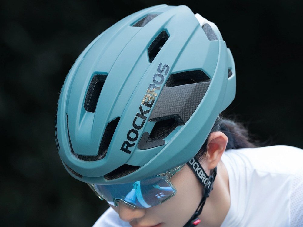 Kask rowerowy Rockbros LK-15 w kolorze jasnoniebieskm na głowie rowerzystki, ujęcie z boku, na tle zieleni.
