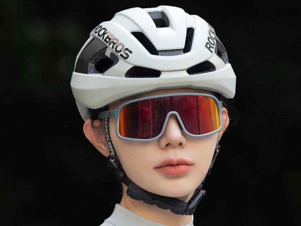 Kobieta w białym kasku rowerowym Rockbros LK-15 i okularach z czerwonymi szkłami, ujęcie z przodu na ciemnym tle.