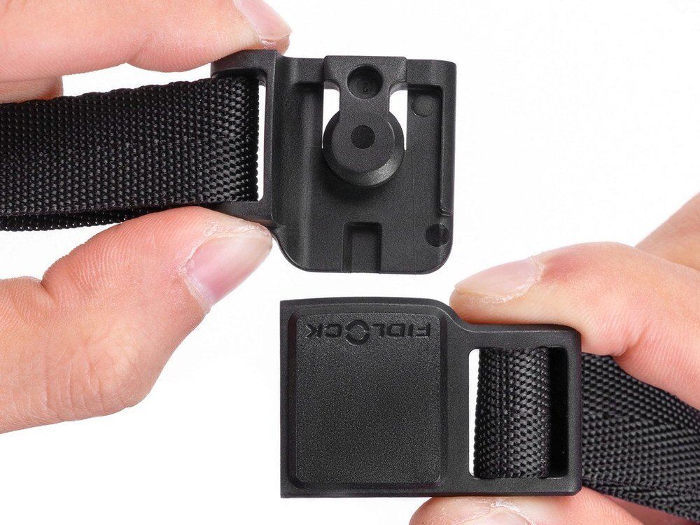 Dwie dłonie trzymające rozłączone elementy magnetycznej klamry Fidlock kasku rowerowego na białym tle, z widocznymi szczegółami mechanizmu.