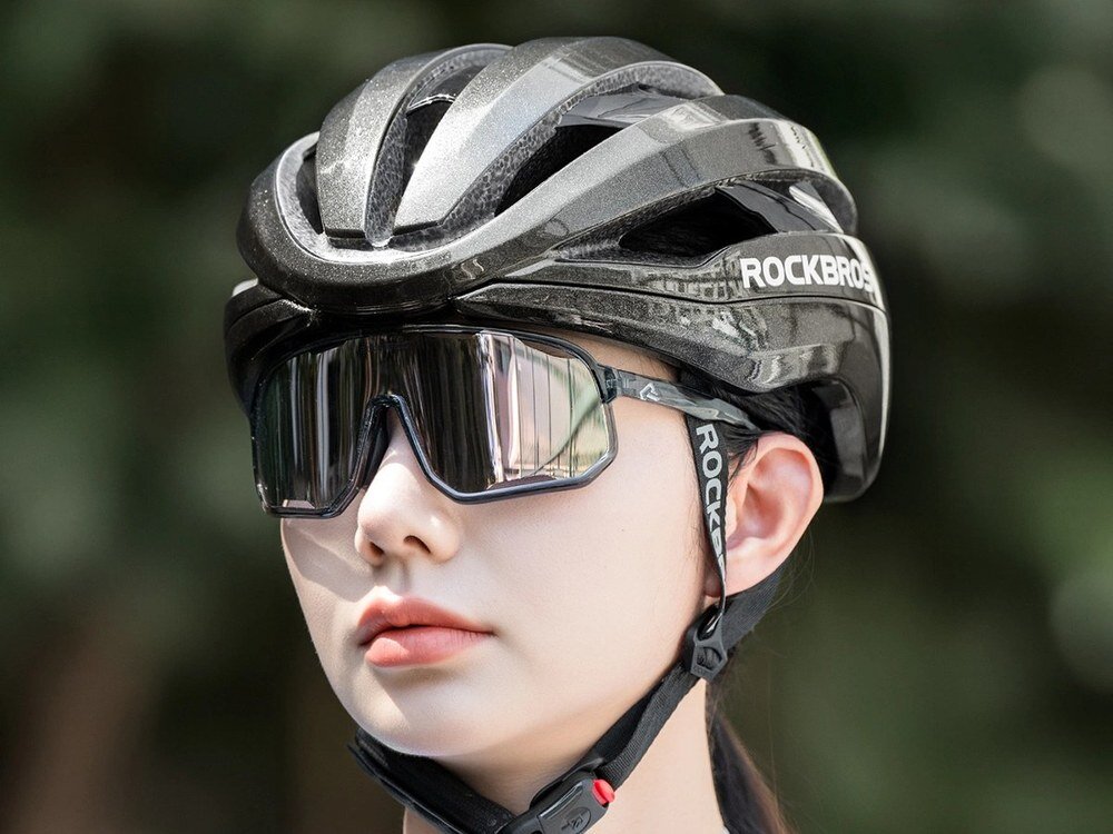 Osoba nosi szary kask rowerowy z napisem ROCKBROS oraz okulary przeciwsłoneczne. Tło jest rozmyte, co podkreśla główny obiekt na pierwszym planie.
