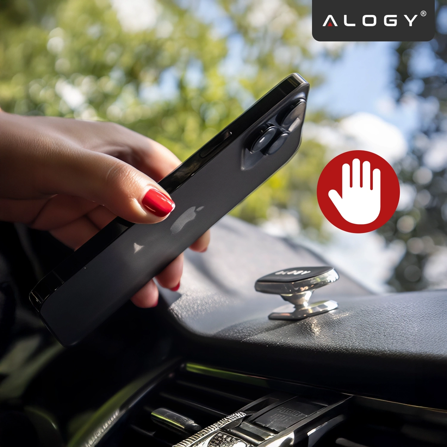 Osoba trzyma telefon nad srebrnym uchwytem magnetycznym zamontowanym na desce rozdzielczej samochodu. W lewym górnym rogu widoczne jest logo \'ALOGY\', a obok telefonu znajduje się czerwony symbol dłoni na białym tle.