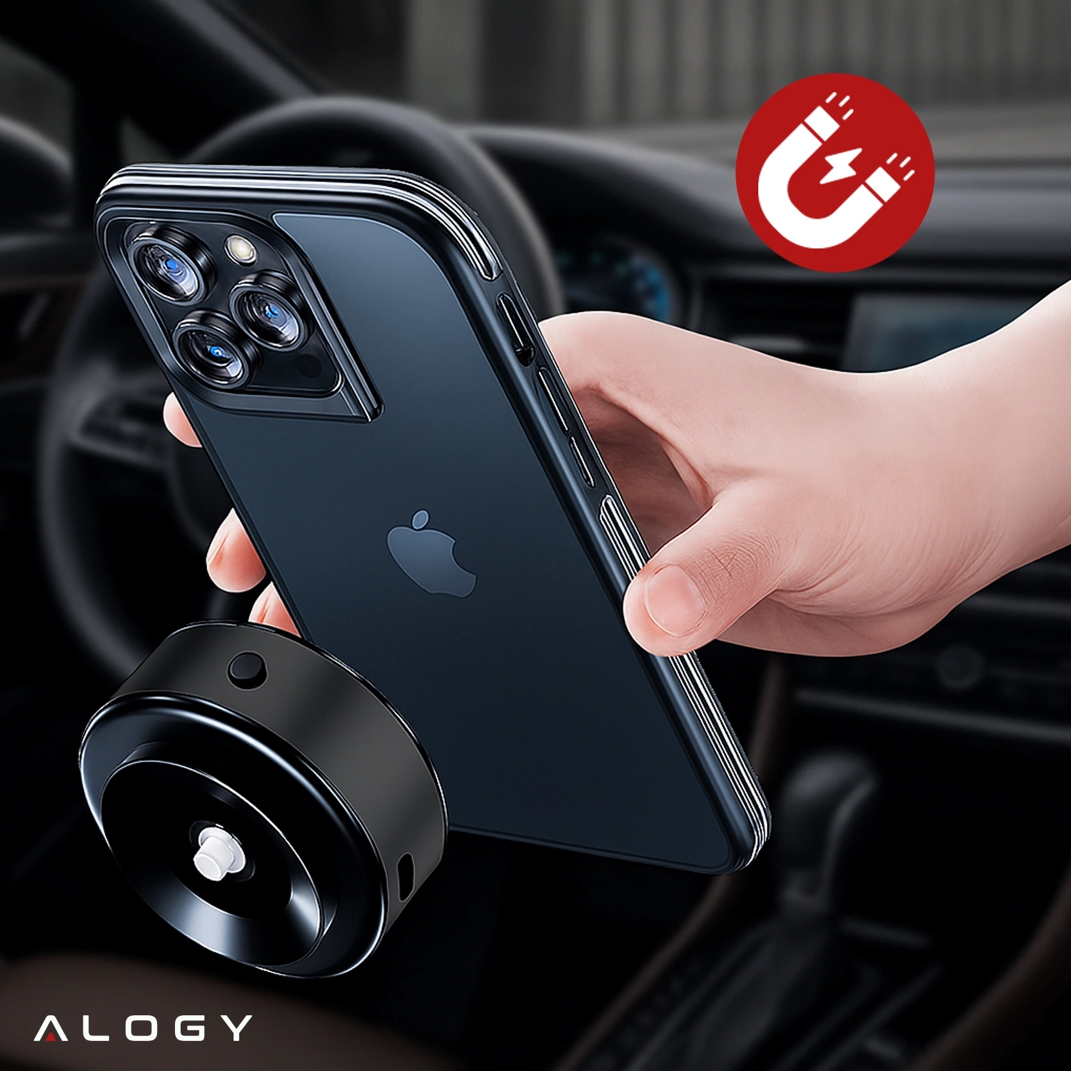 Osoba trzyma telefon z trzema obiektywami aparatu, zbliżając go do czarnego uchwytu magnetycznego. W tle widoczna jest deska rozdzielcza samochodu, a w rogu znajduje się ikona magnesu oraz napis \'ALOGY\'.