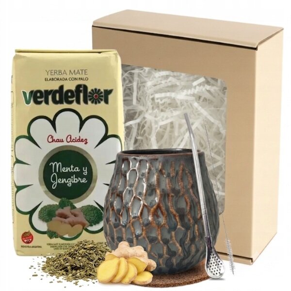 Na obrazie znajduje się opakowanie yerba mate marki verdeflor z napisem \'Menta y Jengibre\', ceramiczne matero o nieregularnej fakturze oraz metalowa słomka. W tle widoczny jest kartonowy zestaw prezentowy z wypełnieniem z białych wiórków papierowych.