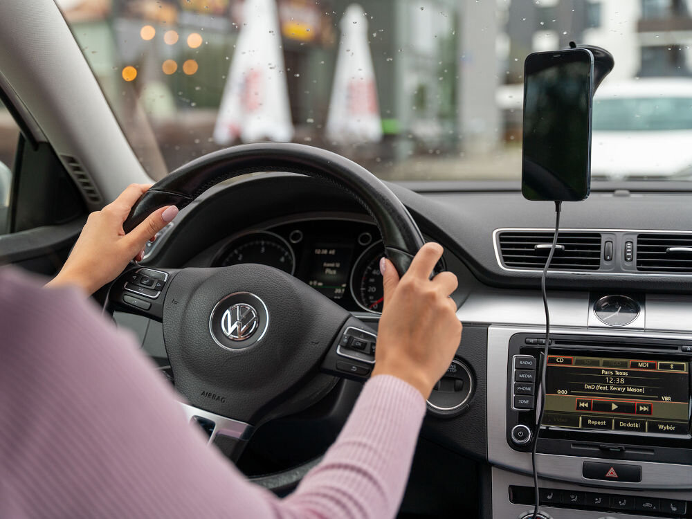 Wnętrze samochodu z zamontowanym uchwytem na telefon na desce rozdzielczej. Na kierownicy widoczne jest logo Volkswagen.