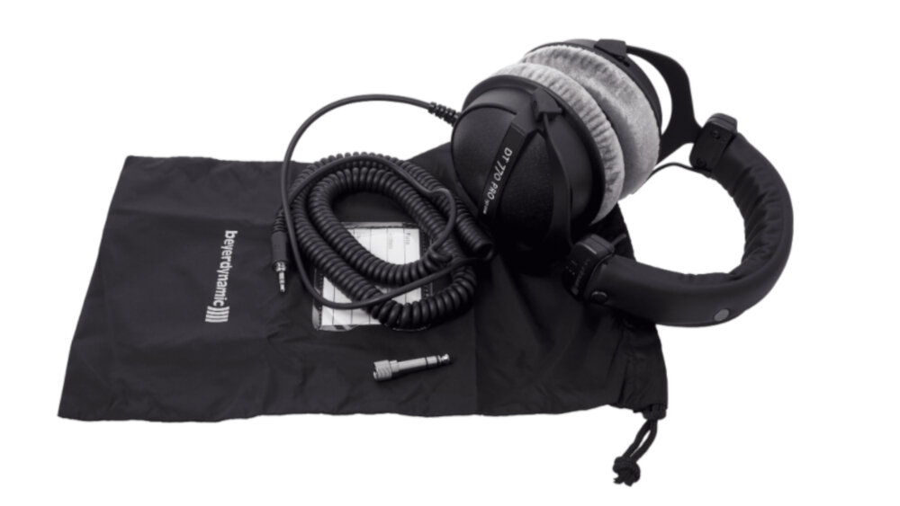 Czarne słuchawki nauszne z szarymi poduszkami leżą na czarnym woreczku z napisem \'beyerdynamic\'. Obok znajduje się spiralny kabel i adapter.