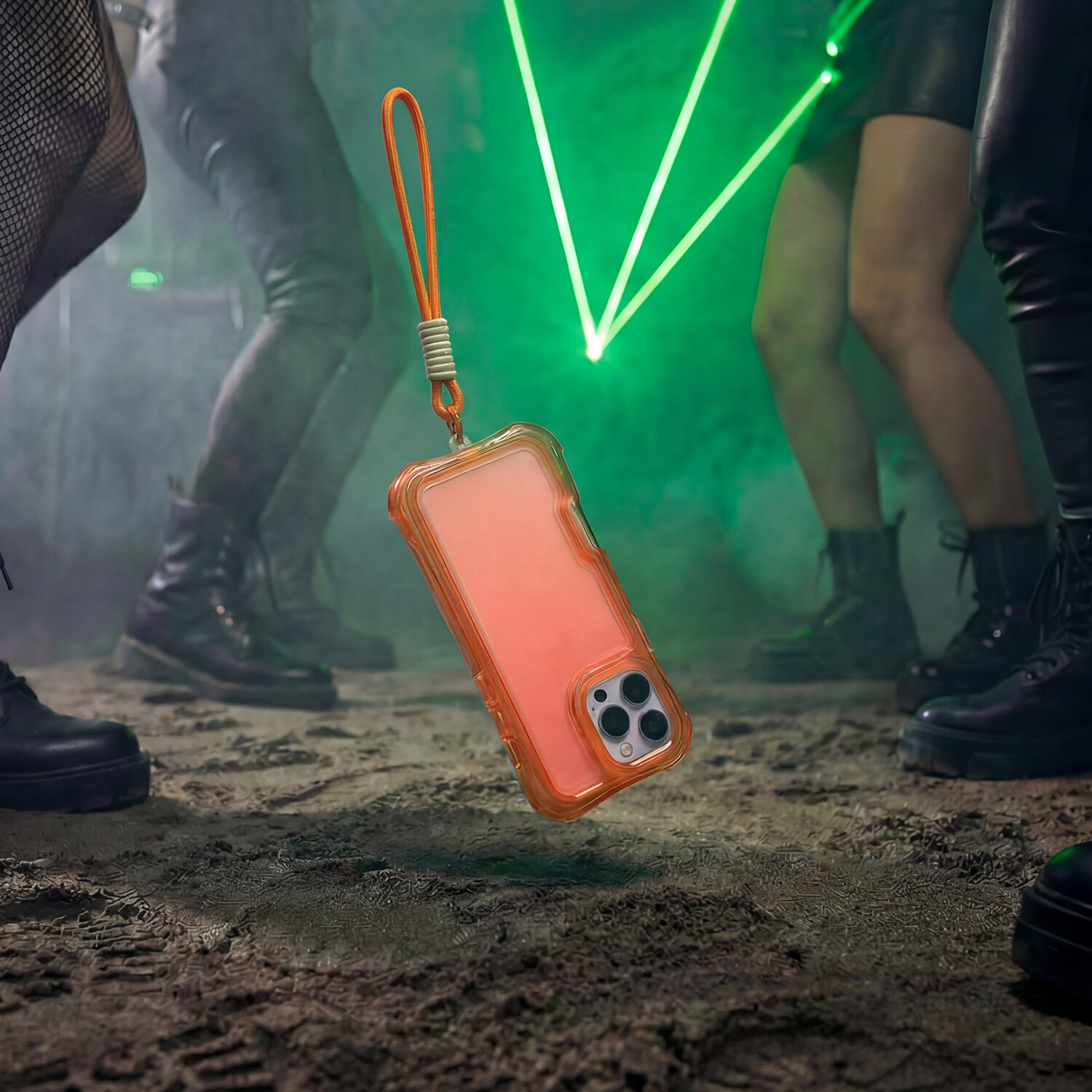 Pomarańczowa nakładka na telefon z dołączoną smyczą unosi się nad ziemią w otoczeniu osób w ciemnym pomieszczeniu z zielonymi laserami.