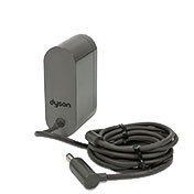 Na obrazie widoczna jest ładowarka z kablem, na której znajduje się logo \'dyson\'. Kabel jest zwinięty obok ładowarki.