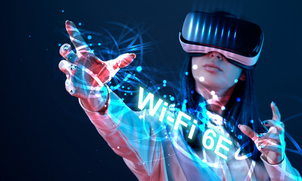 Osoba w goglach VR wyciąga rękę w stronę napisu \'WiFi 6E\' otoczonego niebieskimi efektami świetlnymi.