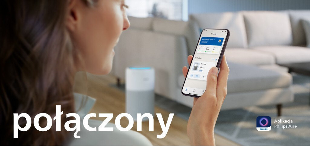 Osoba trzyma smartfon z aplikacją Philips Air+, w tle widoczny jest oczyszczacz powietrza. Na obrazie znajduje się tekst: \'połączony\'.