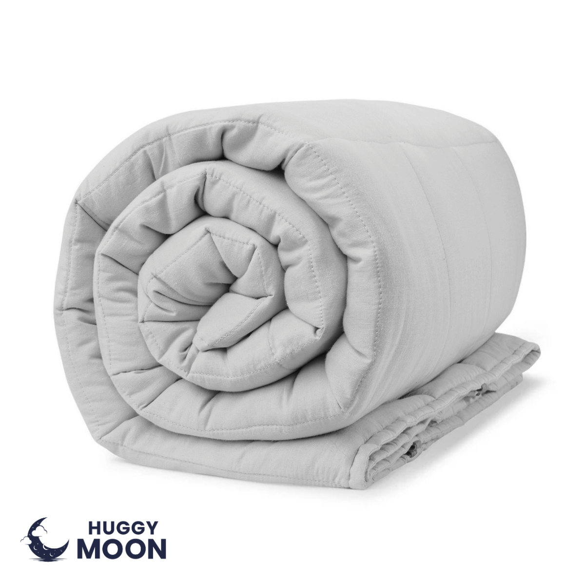 Na obrazie widoczna jest zwinięta, jasnoszara kołdra. W lewym dolnym rogu znajduje się logo z napisem \'HUGGY MOON\'.