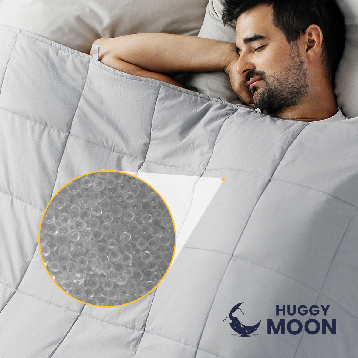 Osoba leży pod szarą kołdrą z widocznym logo \'HUGGY MOON\'. W okrągłym powiększeniu pokazane są przezroczyste kulki wypełniające kołdrę.