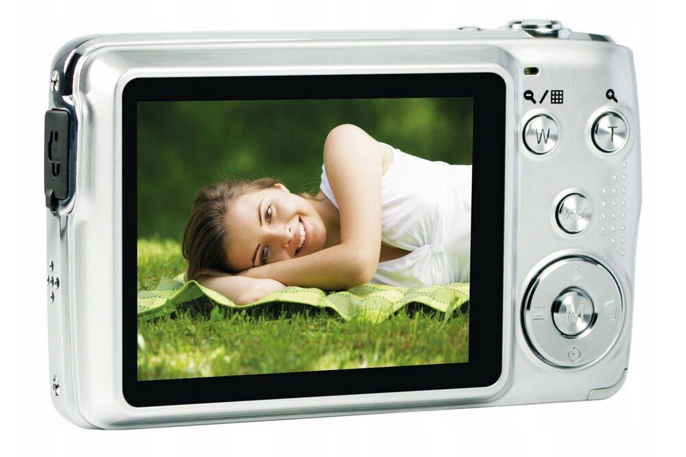 Srebrny aparat fotograficzny z wyświetlaczem LCD, na którym widoczna jest uśmiechnięta osoba leżąca na trawie. Obok ekranu znajdują się przyciski sterujące, w tym przyciski zoomu i menu.
