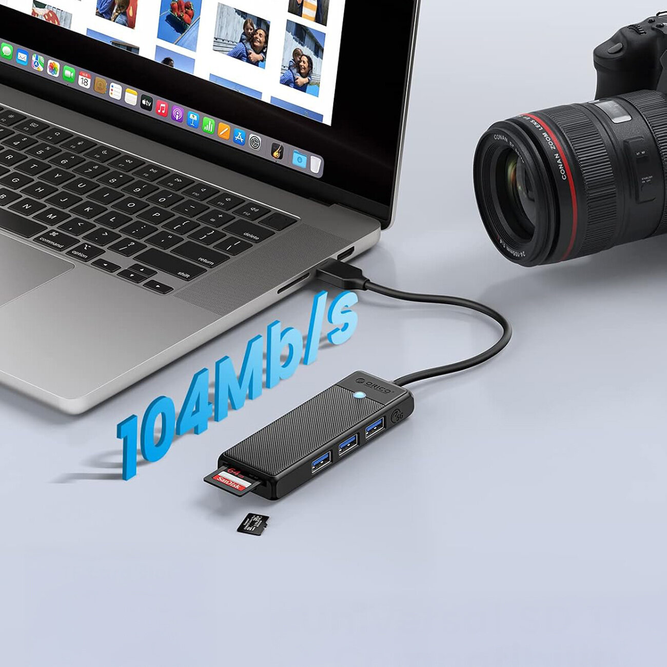 Na obrazie widać laptopa z podłączonym czarnym hubem USB, który ma trzy porty USB-A 3.0 i czytnik kart microSD/SD. Obok huba znajduje się aparat fotograficzny, a nad nim widoczny jest napis \'104Mb/s\'.