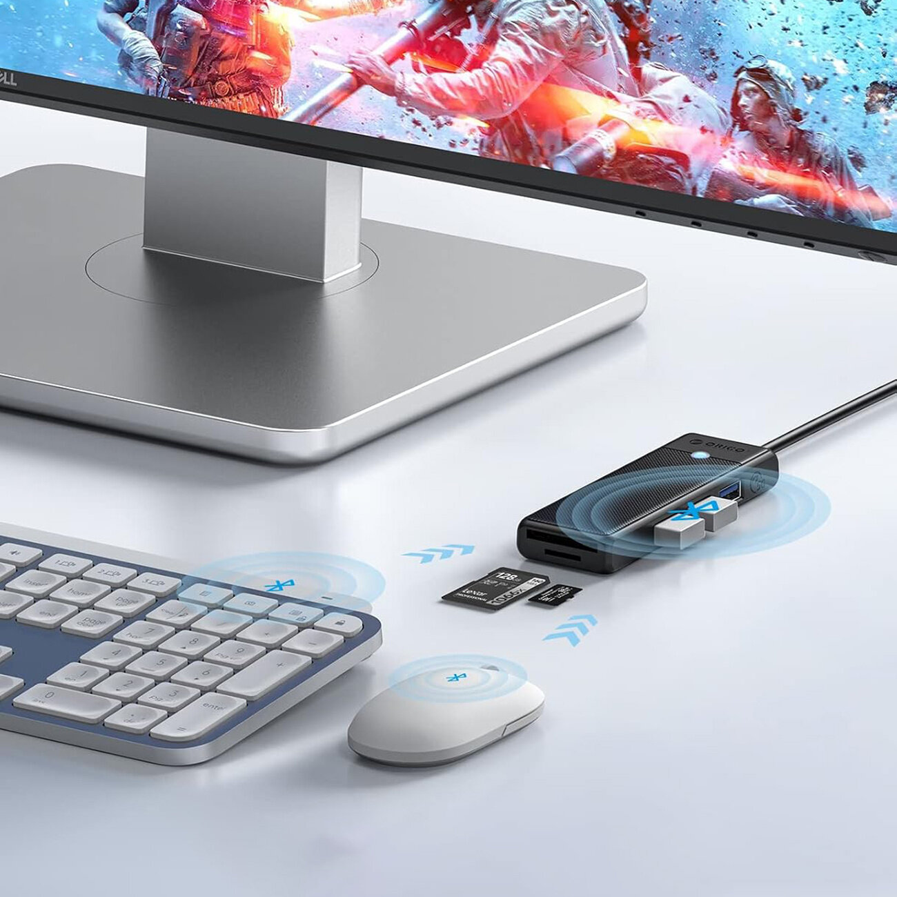 Na biurku znajduje się monitor, klawiatura, myszka oraz czarny hub USB z trzema portami USB-A i czytnikiem kart microSD/SD. Obok huba leżą dwie karty pamięci, a na ekranie monitora widoczna jest dynamiczna scena z gry.
