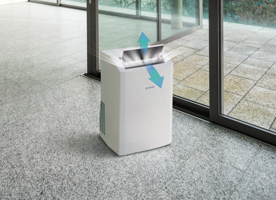 Na obrazie widoczny jest biały klimatyzator przenośny z logo \'gorenje\', ustawiony na podłodze z szarych płytek. Z urządzenia wychodzą niebieskie strzałki wskazujące kierunek przepływu powietrza.