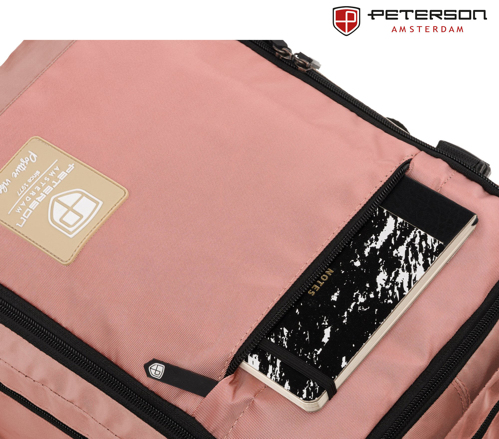 Różowy plecak z widocznym logo \'PETERSON AMSTERDAM\' oraz kieszenią na zamek, w której znajduje się notes z napisem \'NOTE\'.