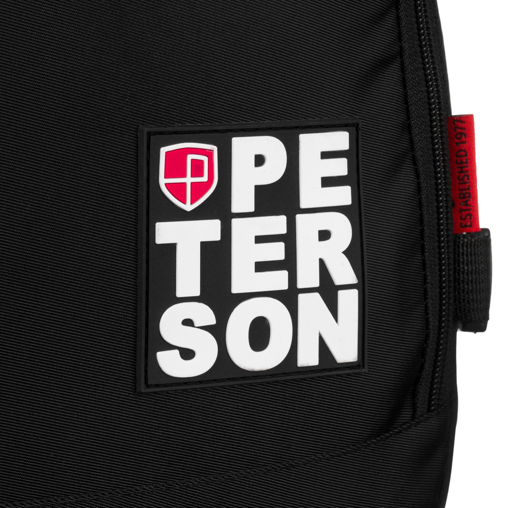 Czarny materiał z naszywką zawierającą napis \'PETERSON\' oraz czerwone logo z literą \'P\'. Obok znajduje się czerwona metka z napisem \'ESTABLISHED 1977\'.