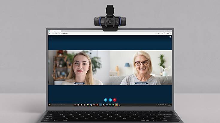 Na obrazie widoczny jest laptop z otwartą aplikacją do wideokonferencji, na ekranie której widać dwie osoby. Na górze laptopa zamontowana jest kamera internetowa.