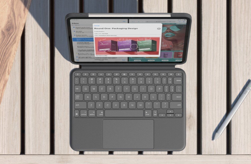 Na drewnianym stole znajduje się szare etui z klawiaturą, w którym umieszczony jest tablet wyświetlający stronę internetową. Obok leży srebrny rysik.