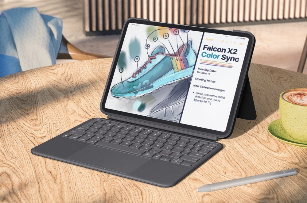 Na drewnianym stole znajduje się iPad Pro w szarym etui z klawiaturą, wyświetlający rysunek buta i tekst \'Falcon X2 Color Sync\'. Obok leży rysik i filiżanka z napojem.