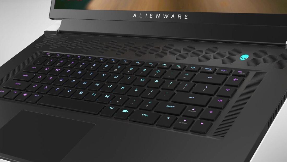 Laptop z widoczną klawiaturą z podświetleniem RGB i logo \'ALIENWARE\' na obudowie. Obok klawiatury znajduje się charakterystyczne logo w kształcie głowy obcego.