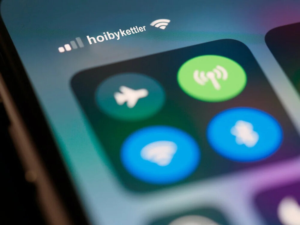 Zbliżenie na ekran smartfona z widocznymi ikonami trybu samolotowego, Wi-Fi, Bluetooth i innych funkcji. Na górze ekranu widoczny jest tekst \'hoibykettler\'.