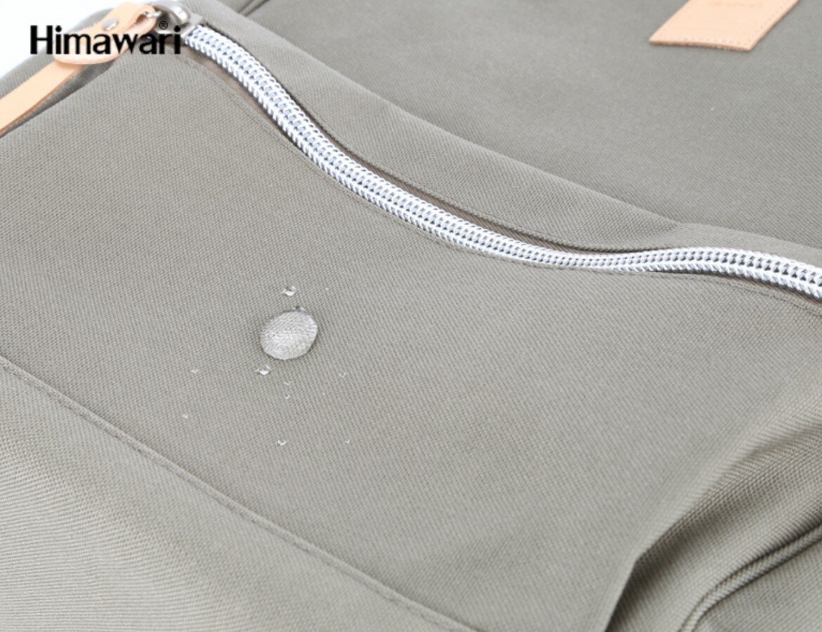 Zbliżenie na materiał plecaka z widoczną kroplą wody oraz zamkiem błyskawicznym. W lewym górnym rogu znajduje się logo \'Himawari\'.