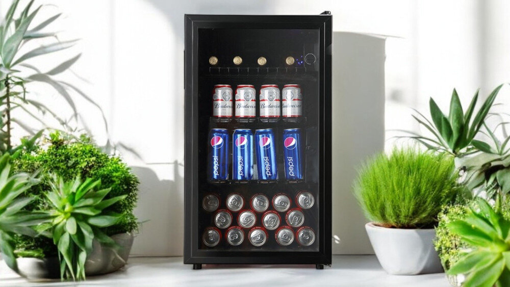 Witryna chłodnicza z przezroczystymi drzwiami, wypełniona puszkami napojów, otoczona roślinami doniczkowymi. Wewnątrz znajdują się puszki Pepsi i Budweiser.