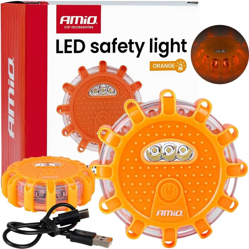 Na obrazie znajduje się pomarańczowa lampa ostrzegawcza z widocznymi diodami LED oraz przyciskiem zasilania, obok której leży kabel USB. W tle widoczne jest opakowanie z napisem \'LED safety light\' oraz logo \'Amio\'.