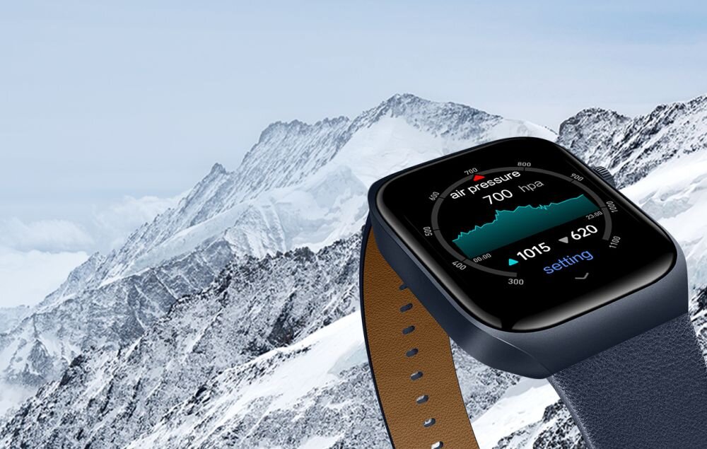 Smartwatch z niebieskim paskiem wyświetla dane dotyczące ciśnienia powietrza na tle ośnieżonych gór. Na ekranie widoczny jest tekst: \'air pressure 700 hpa 1015 620 setting\'.