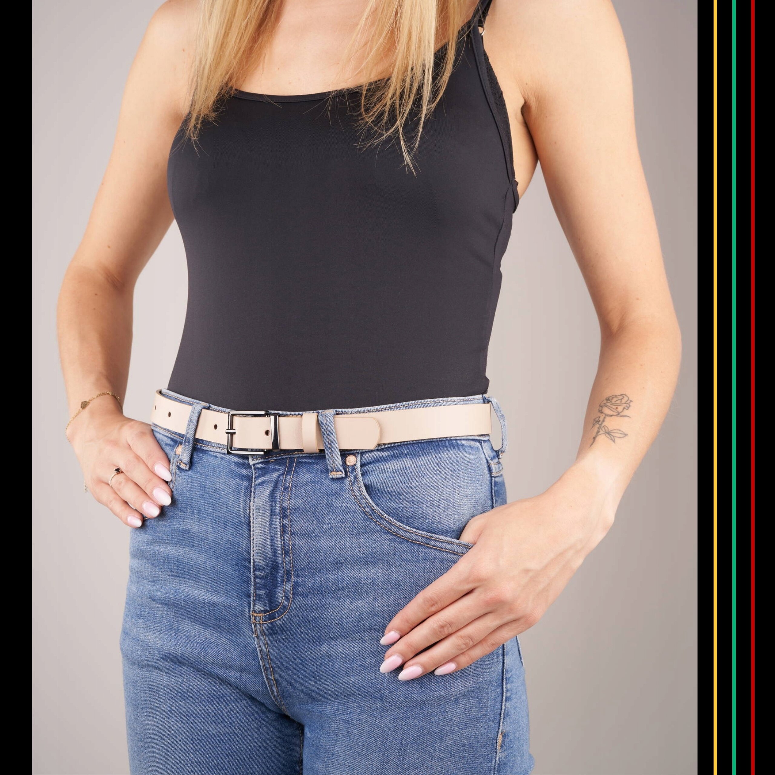Osoba nosi beżowy skórzany pasek włożony w niebieskie dżinsy. Pasek ma klasyczną klamrę i jest dopasowany do eleganckiego stylu.