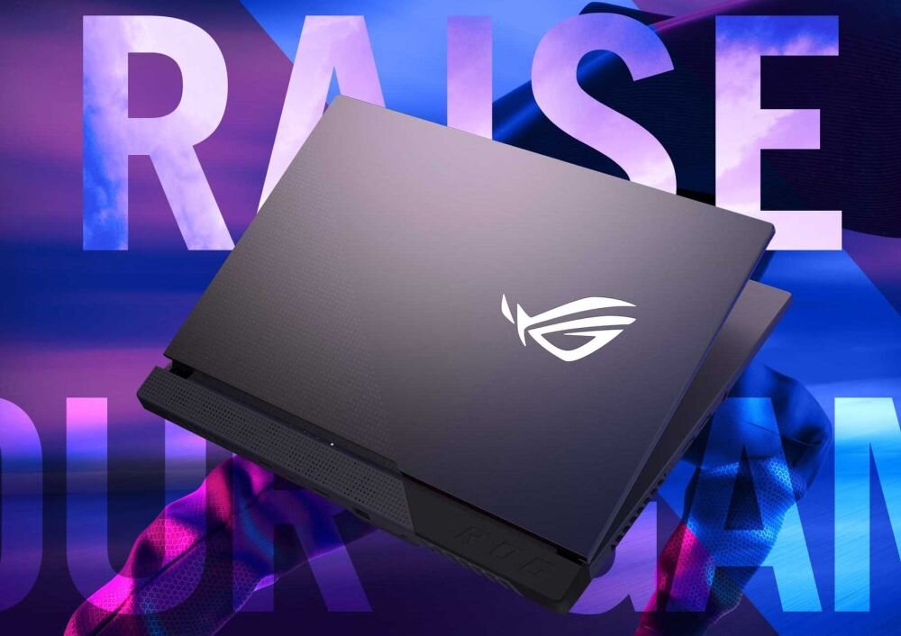 Na obrazie widoczny jest laptop z logo ROG na pokrywie, umieszczony na tle kolorowego napisu \'RAISE YOUR GAME\'.