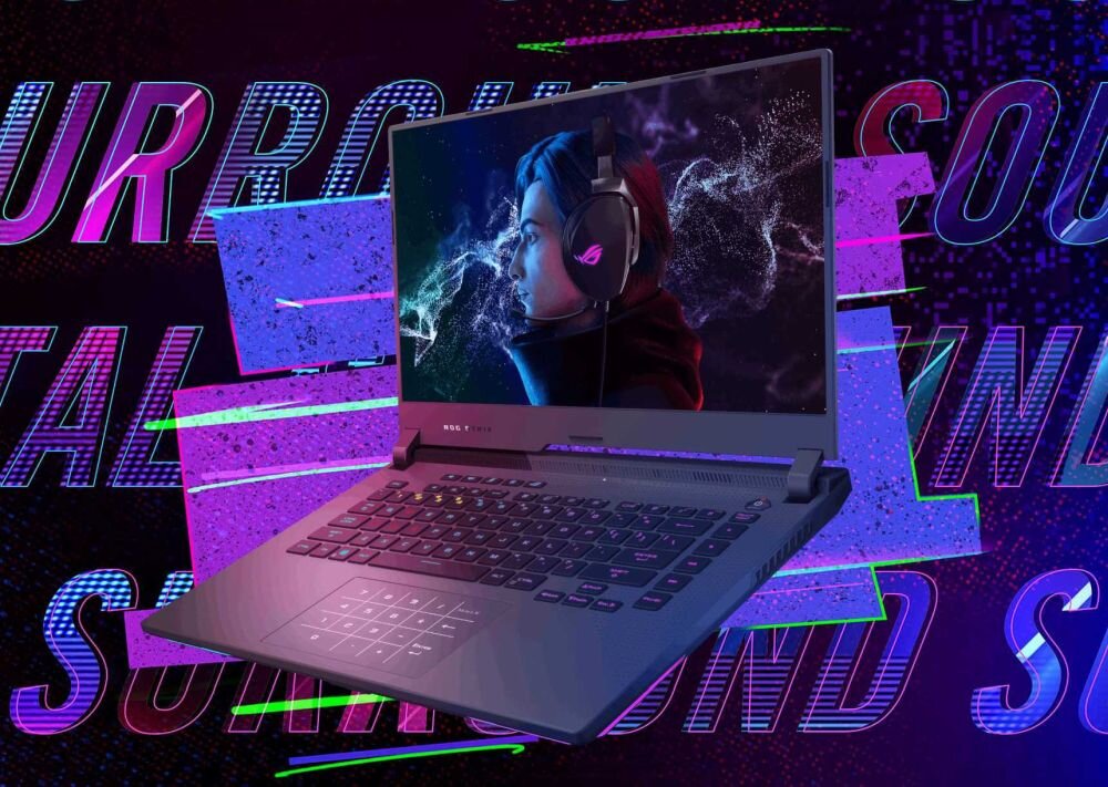Laptop z podświetlaną klawiaturą i ekranem wyświetlającym postać w słuchawkach. W tle widoczne są kolorowe napisy \'SURROUND SOUND\'.