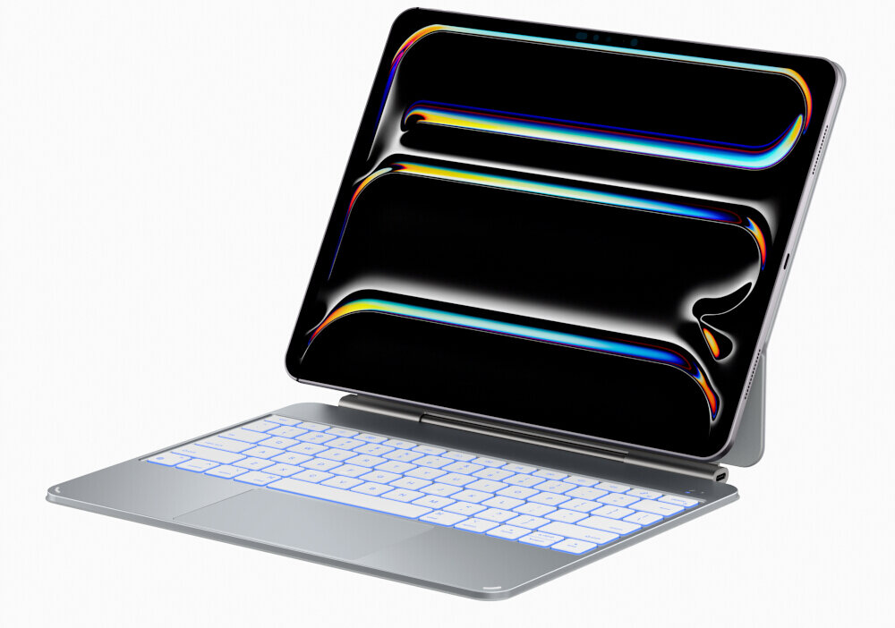 Na obrazie widoczny jest tablet z klawiaturą w srebrnym etui, z wyświetlaczem pokazującym kolorowe wzory na czarnym tle. Klawiatura jest podświetlana na biało.