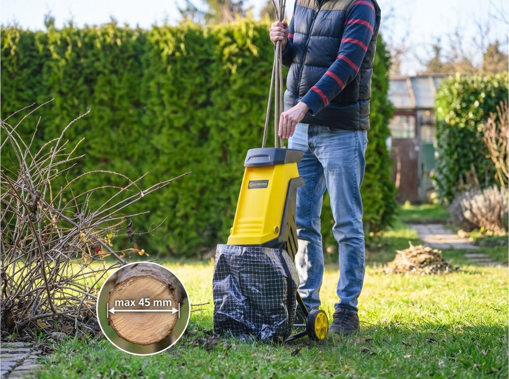 Rozdrabniacz do gałęzi KALTMANN K-RDG-2400 elektryczny 2400W średnica cięcia 45mm, noże, cięcie, ściółka, drewno, Mężczyzna wkładający gałęzie do rozdrabniacza do gałęzi.