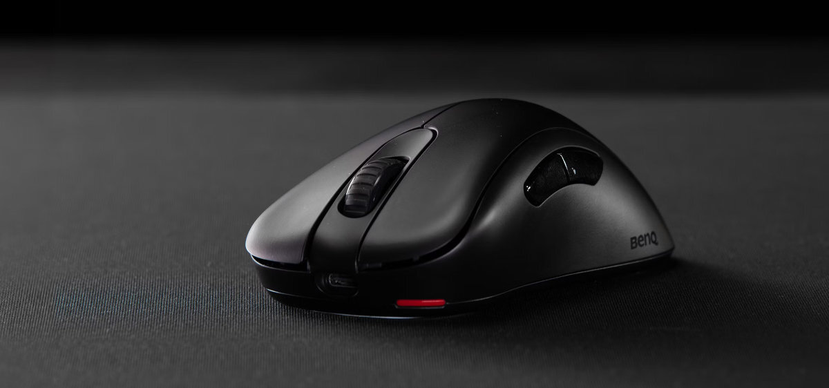 Czarna mysz komputerowa z widocznym logo \'BenQ\' na boku, umieszczona na ciemnej powierzchni. Mysz ma ergonomiczny kształt z wyraźnym przyciskiem i rolką przewijania.
