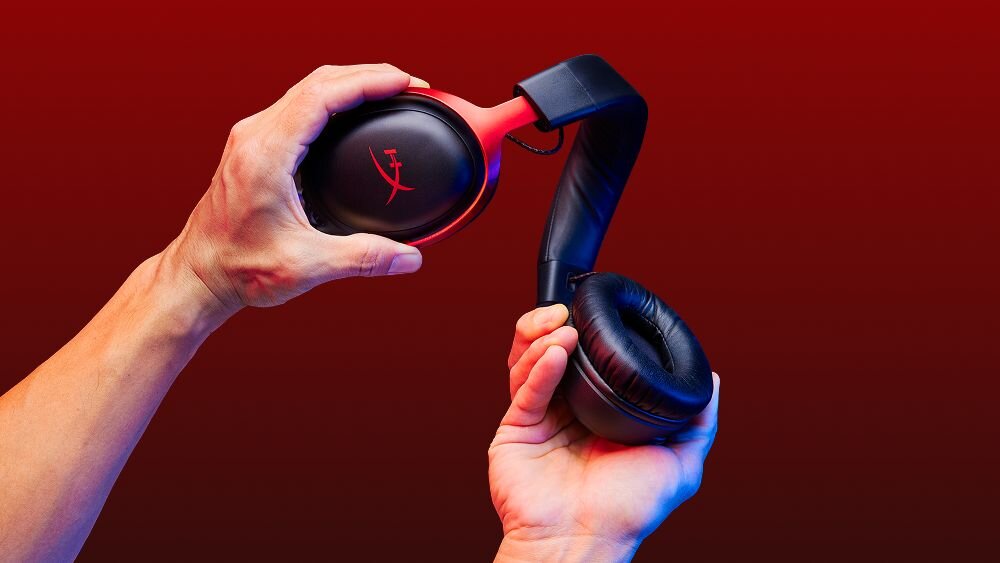 HYPERX Cloud III słuchawki gamingowe, metalowa rama, elastyczna konstrukcja, transport, intensywne użytkowanie, słuchawki trzymane w rękach na czerwonym tle