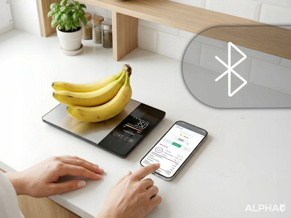 Na blacie kuchennym znajduje się waga kuchenna z bananami, wyświetlająca wagę 350 g. Obok leży smartfon z aplikacją, a w rogu widoczne jest logo Bluetooth i napis ALPHA.