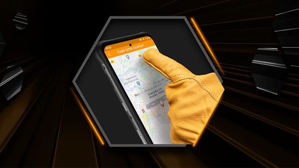 Osoba w żółtej rękawicy dotyka ekranu smartfona, na którym wyświetlana jest mapa z lokalizacjami. Smartfon ma czarną obudowę i widoczne logo \'Hammer\'.