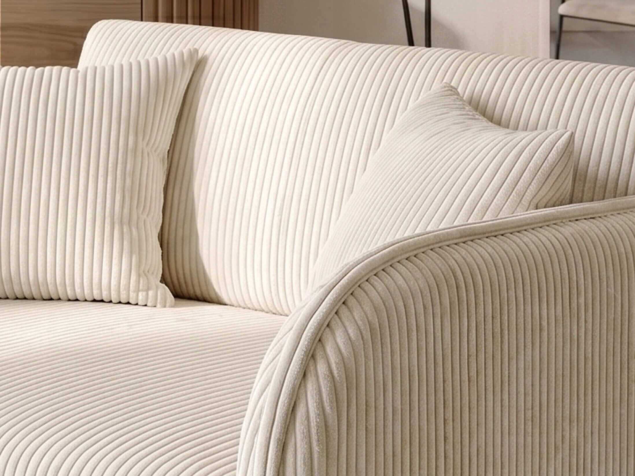 Kremowa sofa z wyraźnym, pionowym prążkowaniem na tapicerce, z dwoma dopasowanymi poduszkami. Sofa ma zaokrąglone krawędzie i elegancki wygląd.